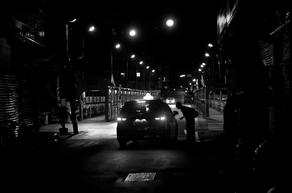 Silhouette of a man interacting with a taxi in a city street at night.